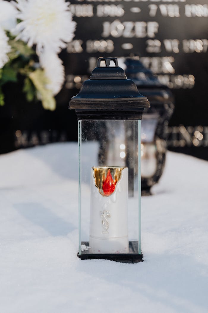 A glass lantern candle on a snow-covered tombstone symbolizes remembrance.